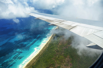 Fototapeta na wymiar Wing of an airplane flying above the clouds over tropical island