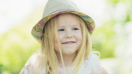 Smiling blond girl in a hat at sunny summer day in the garden.