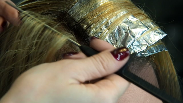 Separation of the locks of hair with an applicator brush. Preparation for highlighting or lowlighting hair. Professional hair coloring process. 