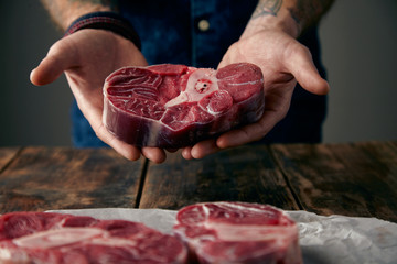 Two tattoed hands offer a piece of great meat steak with bone on
