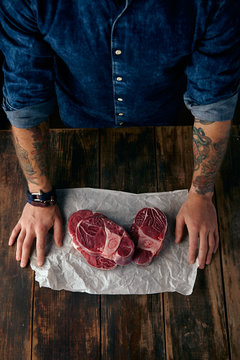 Top view of butcher's tattoed hands and steaks on craft paper