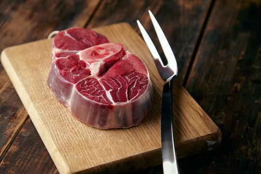 Fresh meat steak with bone on wooden plate with big fork