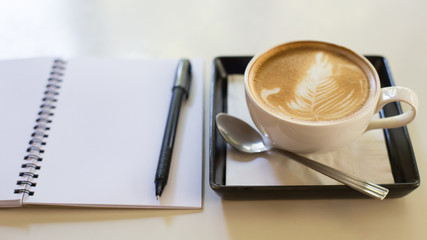 Hot latte art coffee cup on wooden table and note book