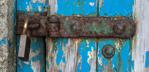 Hasp and padlock on old wooden door with blue flaking paintwork.