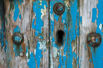 Keyhole in old wooden door, with flaking blue paintwork.