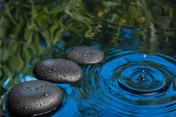 Obraz na płótnie Canvas Three spa stone drops lie in the blue water