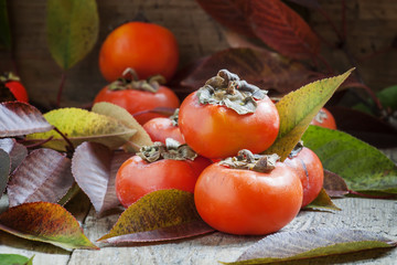 Persimmons with leaves on the old wooden table, selective focus