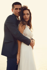 beautiful groom and bride in wedding clothes posing on sea coast