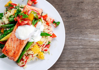 Pan fried Salmon with tender asparagus, courgette served on couscous mixed with sweet tomato, yellow pepper, with greek yogurt on old wooden table.