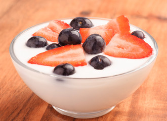 bowl full of yogurt with blueberries and strawberries on wood