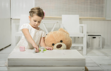 Expressive beautiful little girl having a tea party with her teddy bear. 