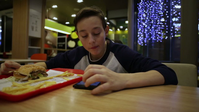 Teen Eating French Fries and Using Smartphone