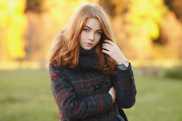 Outdoors portrait of young beautiful redhead woman in scarf and jacket on yellow autumn foliage background