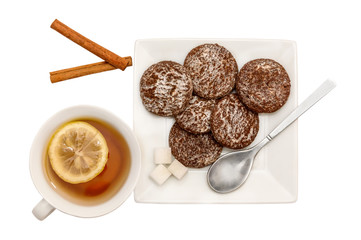 A cup of tea with sugar cubes, lemon, cinnamon and cookies on a
