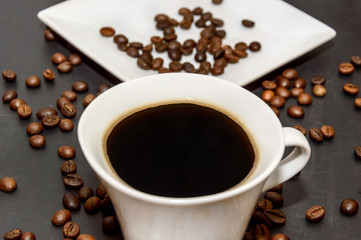 cup of coffee and saucer with coffee beans on blackboard