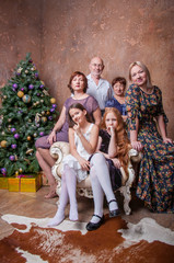 Fototapeta na wymiar Большая семья с бабушкой, дедушкой, мамами и девочками сидят около новогодней елки