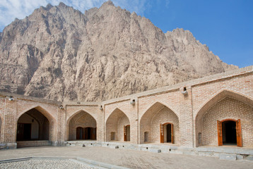 Mountain behind the historical brick walls of persian caravanserai with wide empty courtyard under the sun - obrazy, fototapety, plakaty