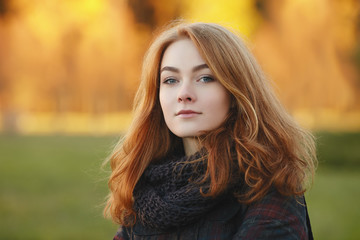 Closeup portrait of young emotional redhead woman  in scarf and plaid jacket with blurred autumn foliage background outdoors