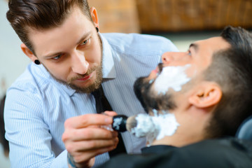 Obraz na płótnie Canvas Professional barber shaving the beard of his client 
