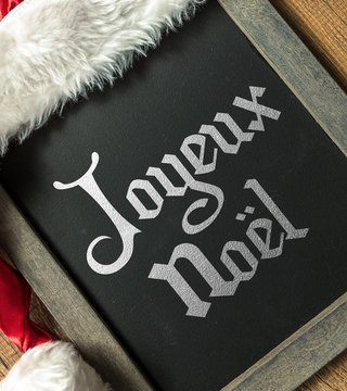 Merry Christmas (In French) written on blackboard with santa hat