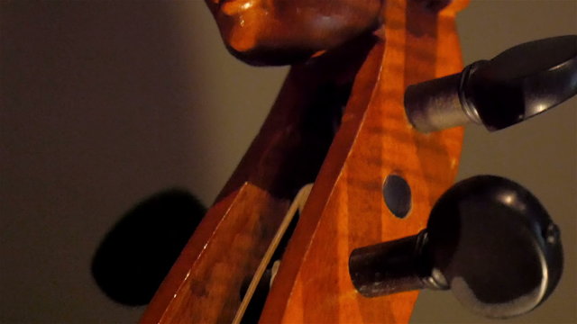 Carvings on the tip of a violin in a room. The image of a woman that is carved on the wooden violin