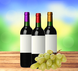 bottles of red wine and grape on wooden table over bright nature