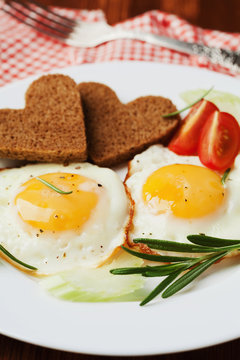Fried eggs with fresh vegetables and toast in shape of heart on white plate, delicious Breakfast