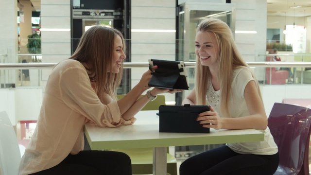 two girls in intertainment center speaks and look in the tablet