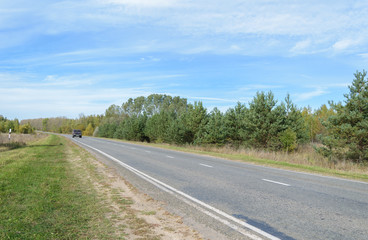 Fototapeta na wymiar Suburban asphalt highway with white intermittent markings and a car