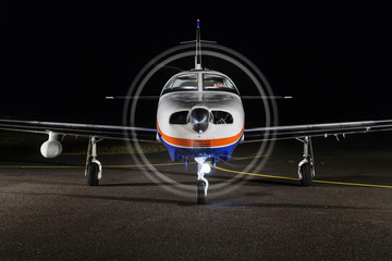 The small single-engine piston aircraft on the runway, illuminated with propeller