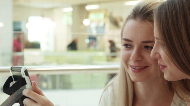 two girls in intertainment center speaks and look in the tablet