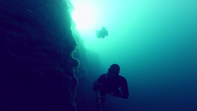 Deep Freedivers Exploring a side of a Underwater Cliff into a Quarry