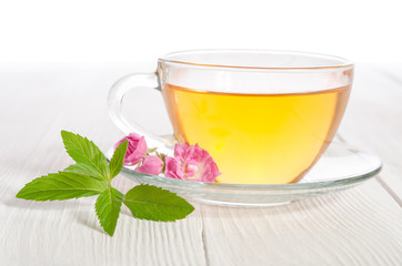 Glass cup of tea with mint and  rose on white wooden table
