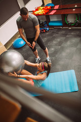 Woman exercising with her fitness instructor at the fitness center with pilates ball