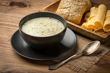 Cheese soup in a black plate on the rustic wooden background.