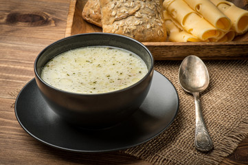 Cheese soup in a black plate on the rustic wooden background.