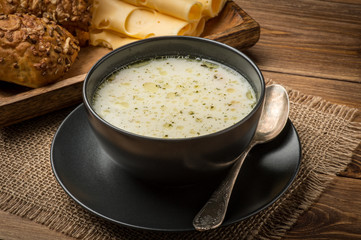 Cheese soup in a black plate on the rustic wooden background.