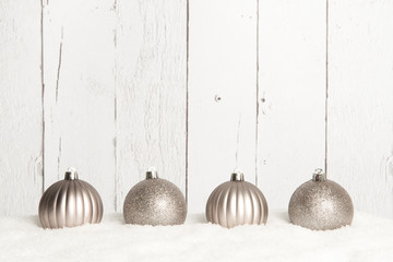 Silver christmas ball ornaments lying on snow on a white wooden background