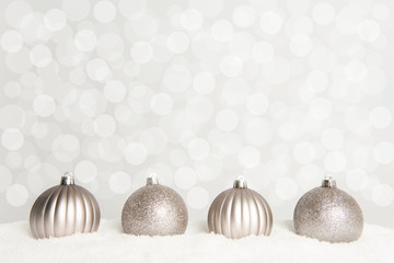 Silver christmas ball ornaments lying on snow on a grey bokeh background 