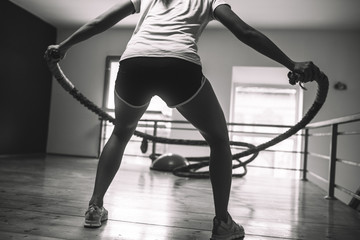 A determined female gym-goer works up a sweat while energetically using battle ropes, pushing her...