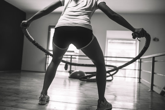 A determined female gym-goer works up a sweat while energetically using battle ropes, pushing her limits to build strength and improve her overall fitness.