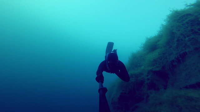 Deep Freedivers Exploring a side of a Underwater Cliff into a Quarry