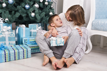Happy mother and son in pajamas sitting with a gift near the Chr