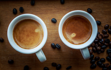 Two espresso coffees in small white cups,with a coffee bean rest