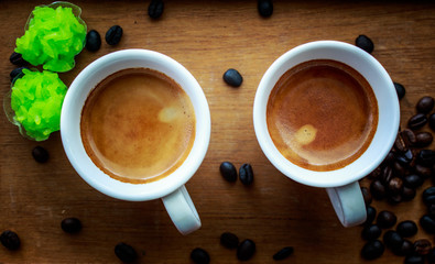 Two espresso coffees in small white cups,with a coffee bean rest