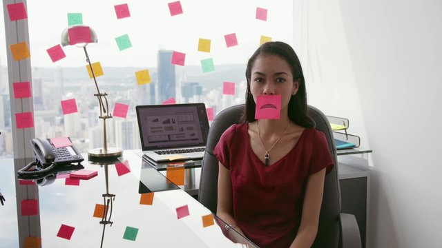 Latin american woman working as secretary in modern office with beautiful sight on the city, sticking adhesive notes with tasks on window. The girl holds a note with sad emoticon on mouth.