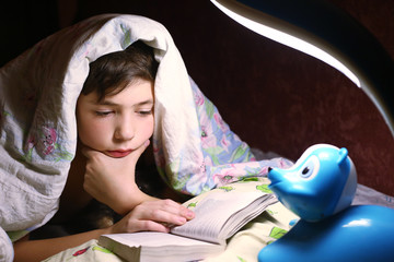 boy  reading book under the blanket in night hour