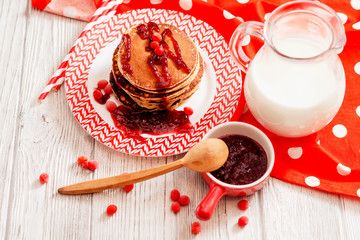 
hearty breakfast, sweet American pancakes with raspberry , cherry or strawberry jam , berries and milk on a wooden background