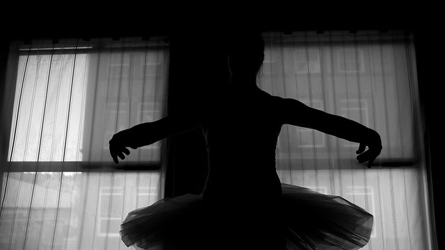Black and white silhouette of a ballerina dancing in front of a window
