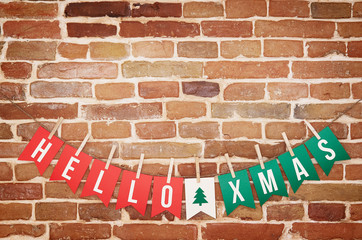 Red and green HELLO XMAS and twig tree paper card DIY flag garland decoration on rustic brick wall background postcard.